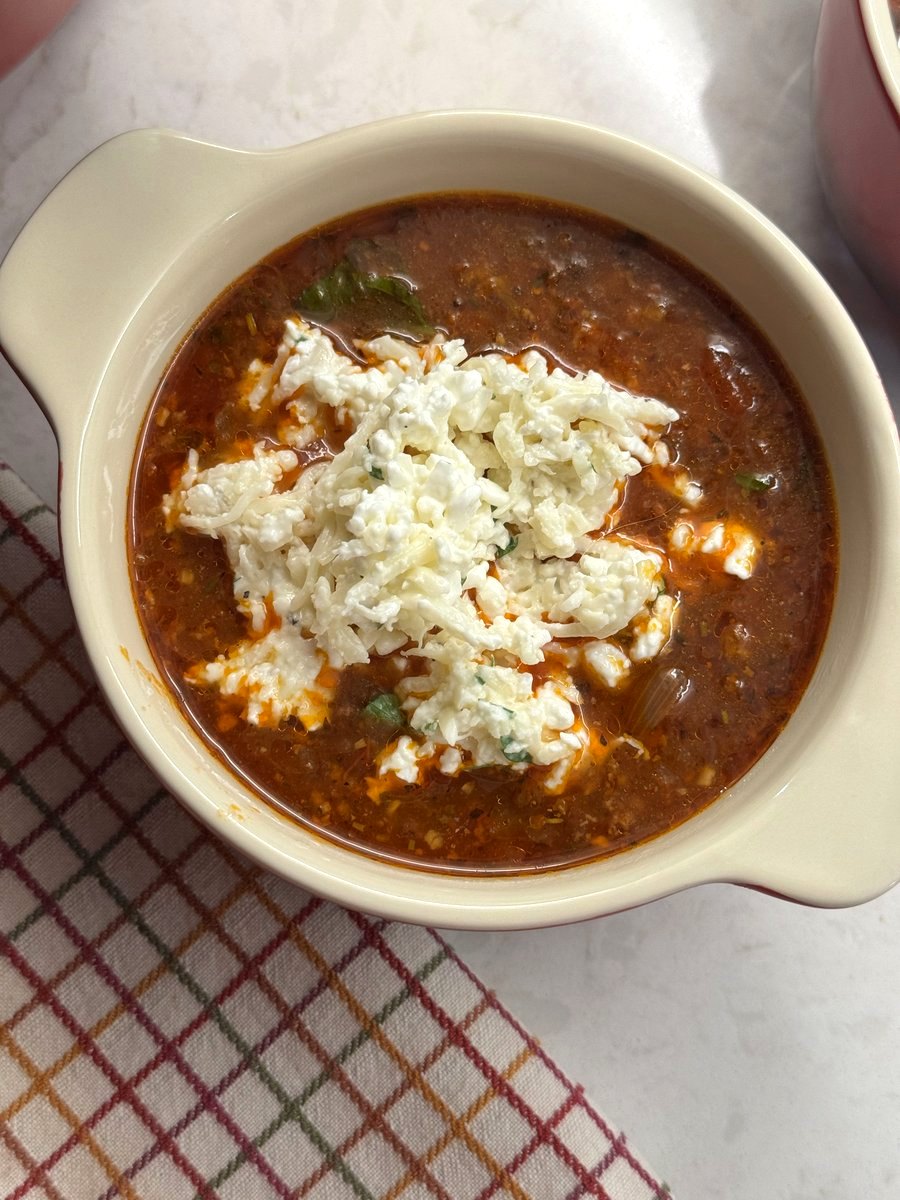 Overhead view of a bowl of lasagna soup with a mound of cheese topping and a fresh basil leaf