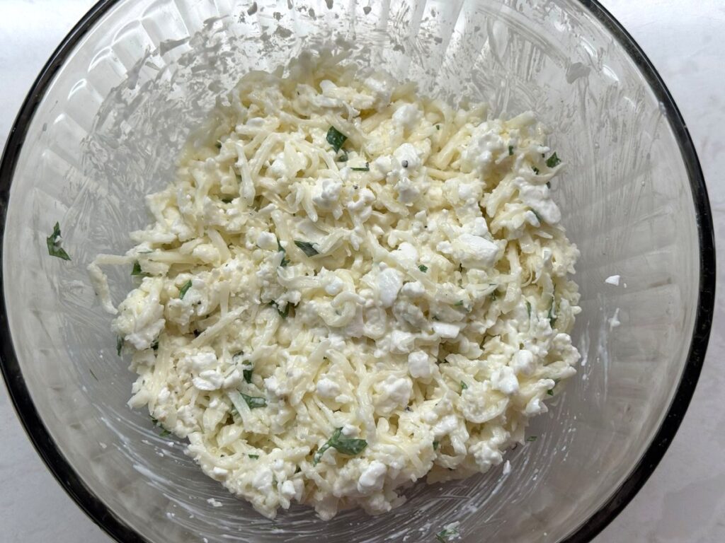 The cottage cheese, mozzarella, parmesan, and parsley topping stirred together in a glass bowl