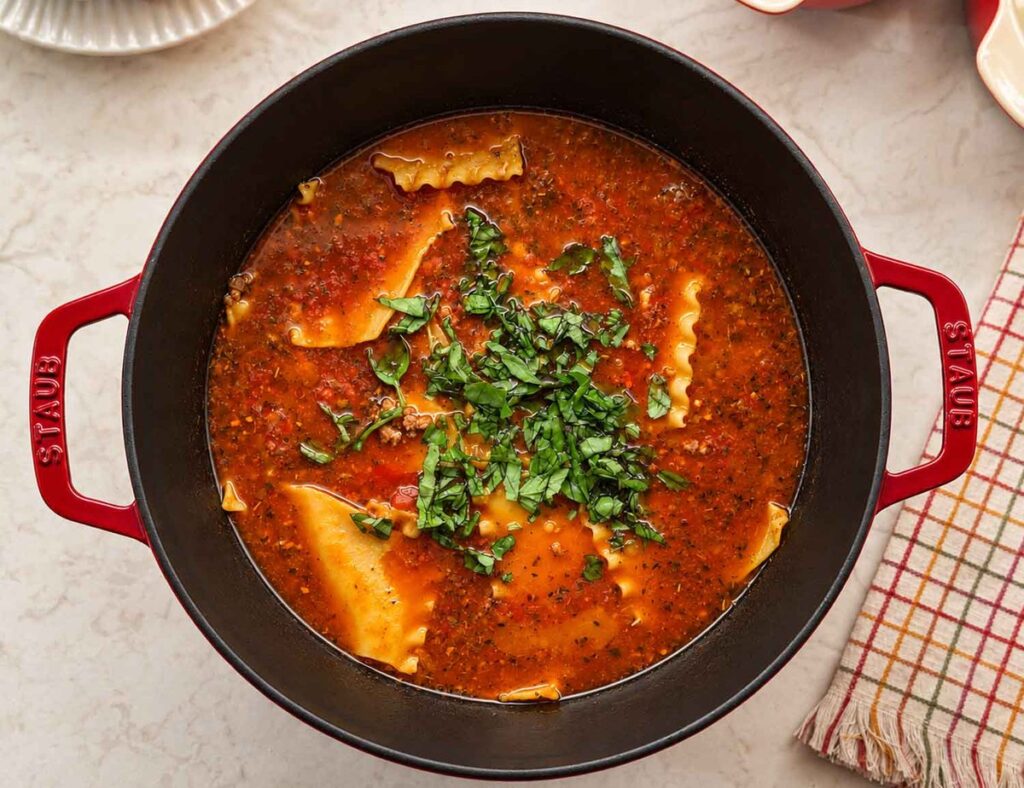 Overhead view of lasagna soup in a red Dutch oven with tender ruffled lasagna noodles