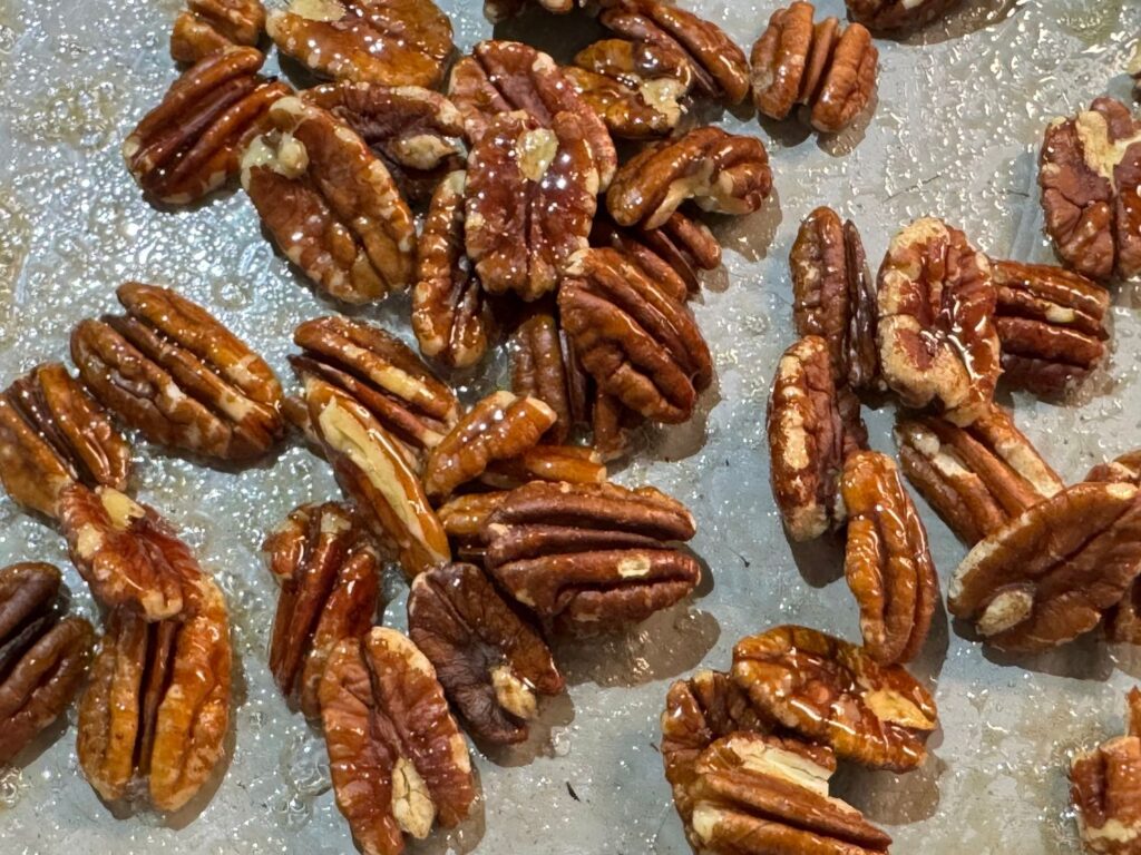 Pecans coated in sticky maple syrup in a skillet