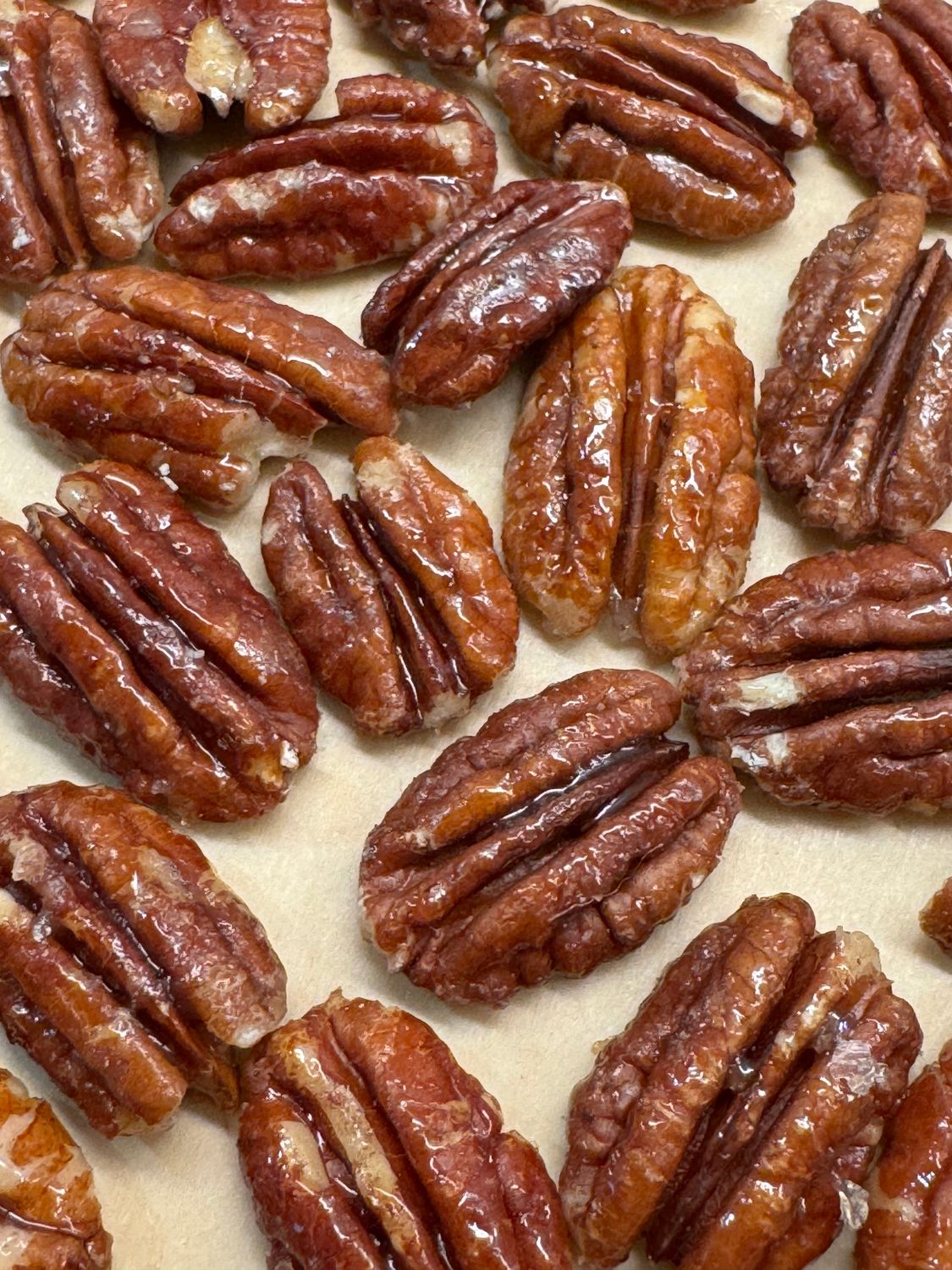 Glossy maple pecans spread out on parchment paper to cool