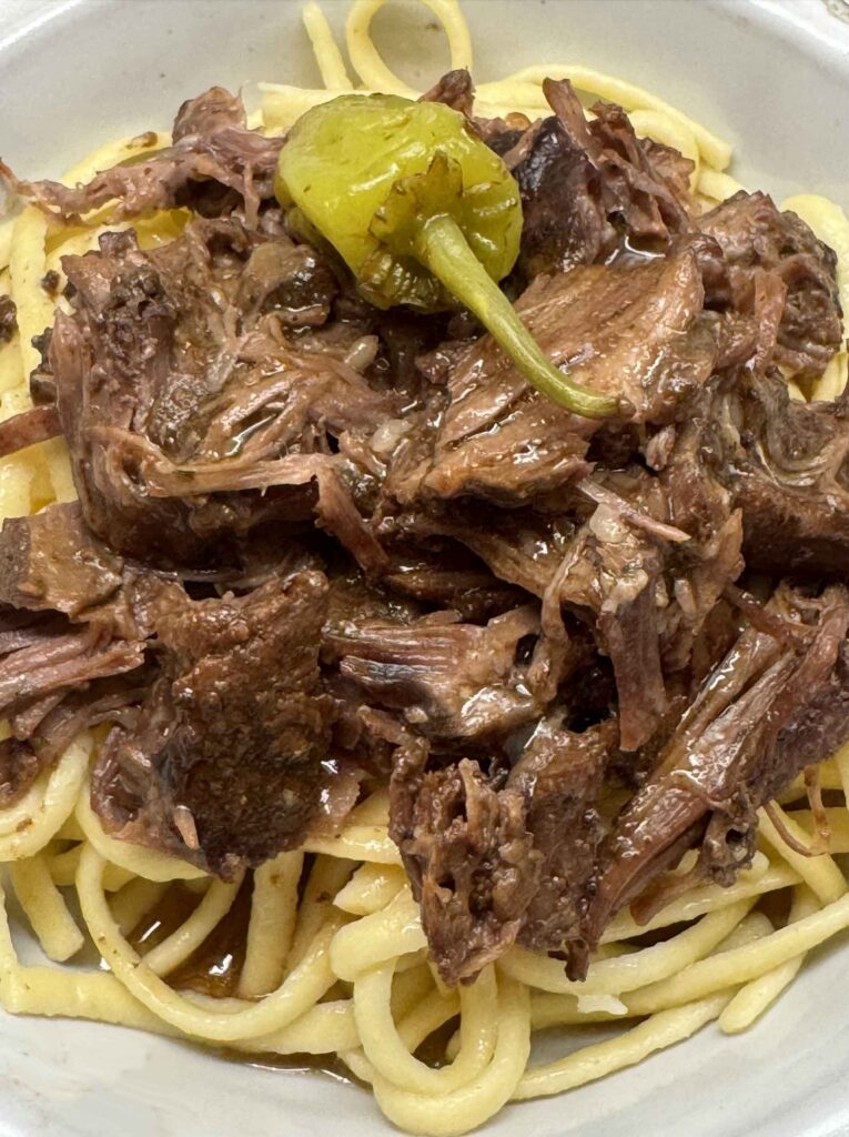 Closeup of a bowl of Mississippi pot roast with a pepperoncini on top