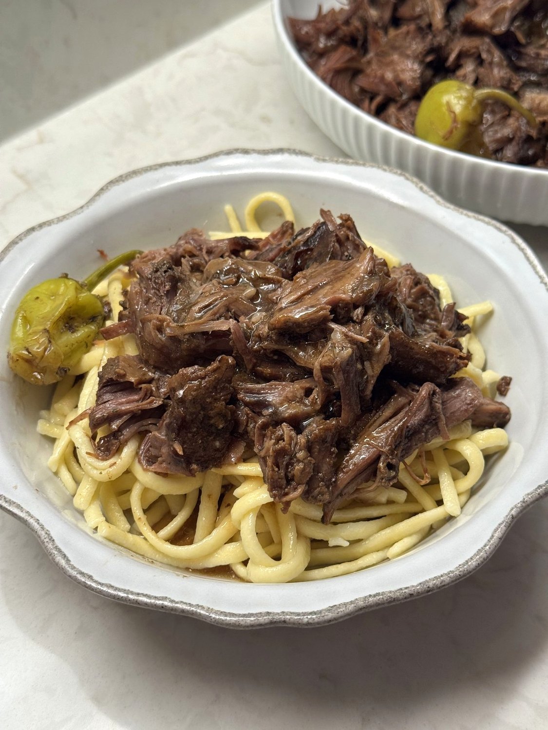 Mississippi pot roast with a pepperoncini piled over spaetzle in a white bowl