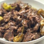 Shredded Mississippi pot roast with whole pepperoncini in a white bowl