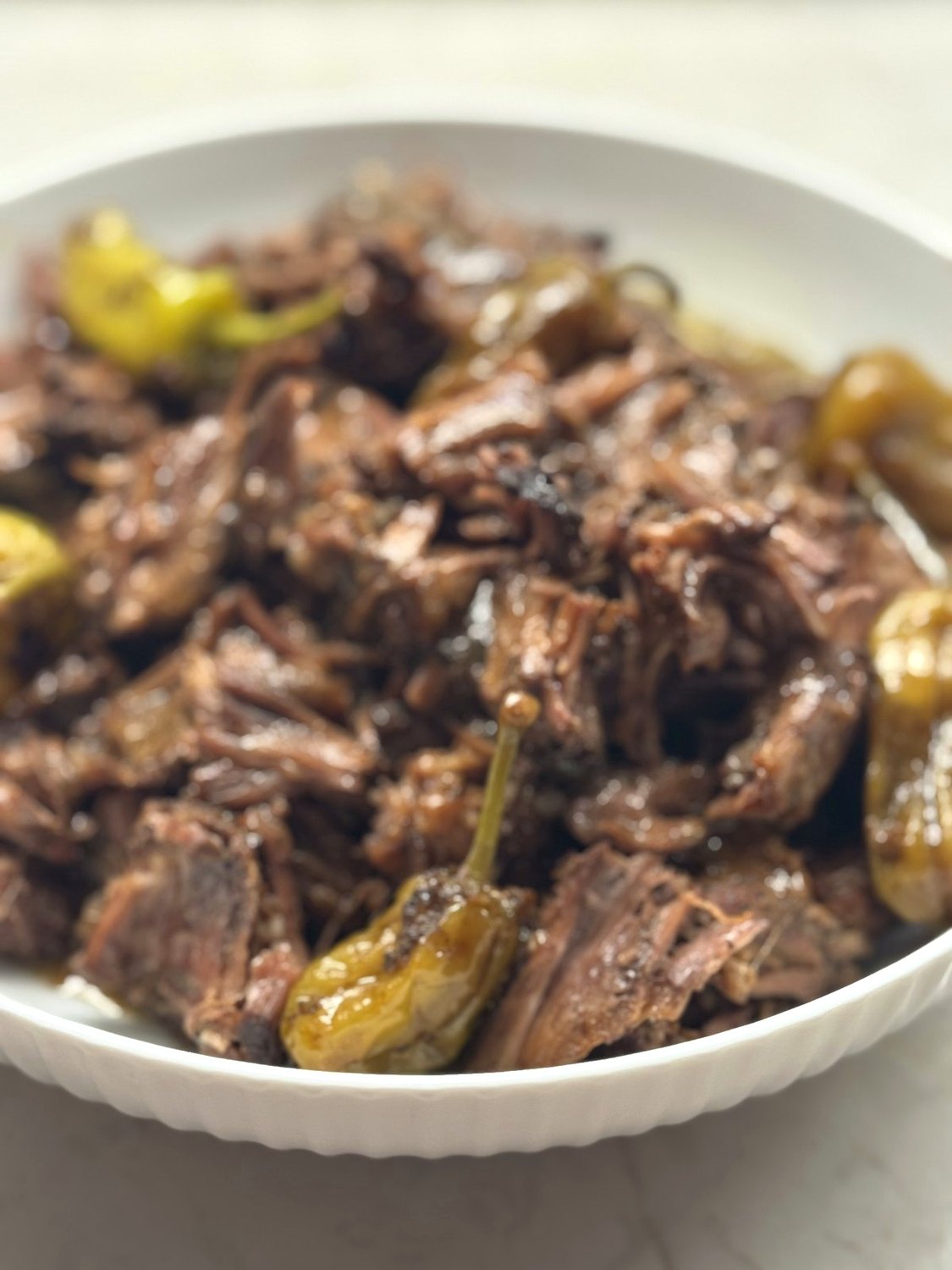 Shredded Mississippi pot roast with whole pepperoncini in a white bowl
