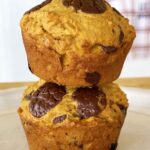 Two pumpkin chocolate chip muffins stacked on a white plate, with melted chocolate on top
