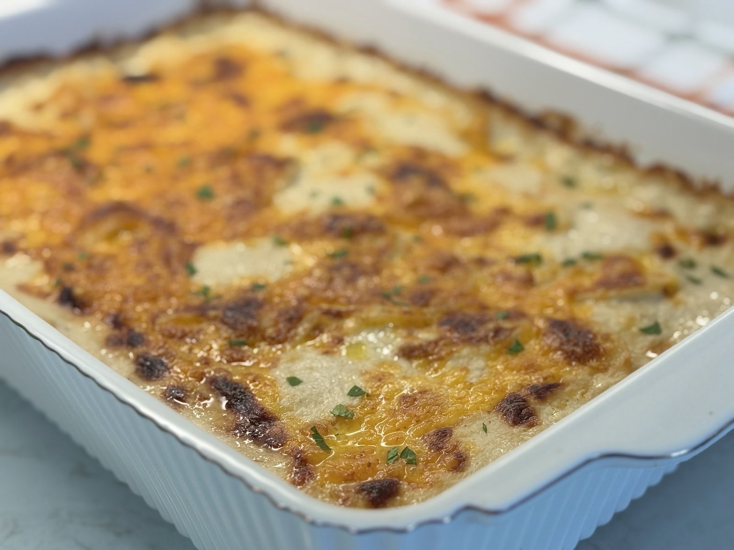 Saucy scalloped potatoes with a golden, browned cheddar top in a white baking dish