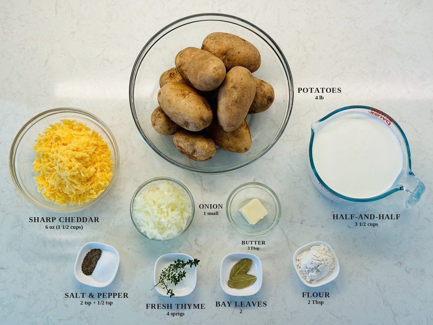 Labeled ingredients for scalloped potatoes: russet potatoes, sharp cheddar, half-and-half, onion, butter, salt and pepper, fresh thyme, bay leaves, and flour
