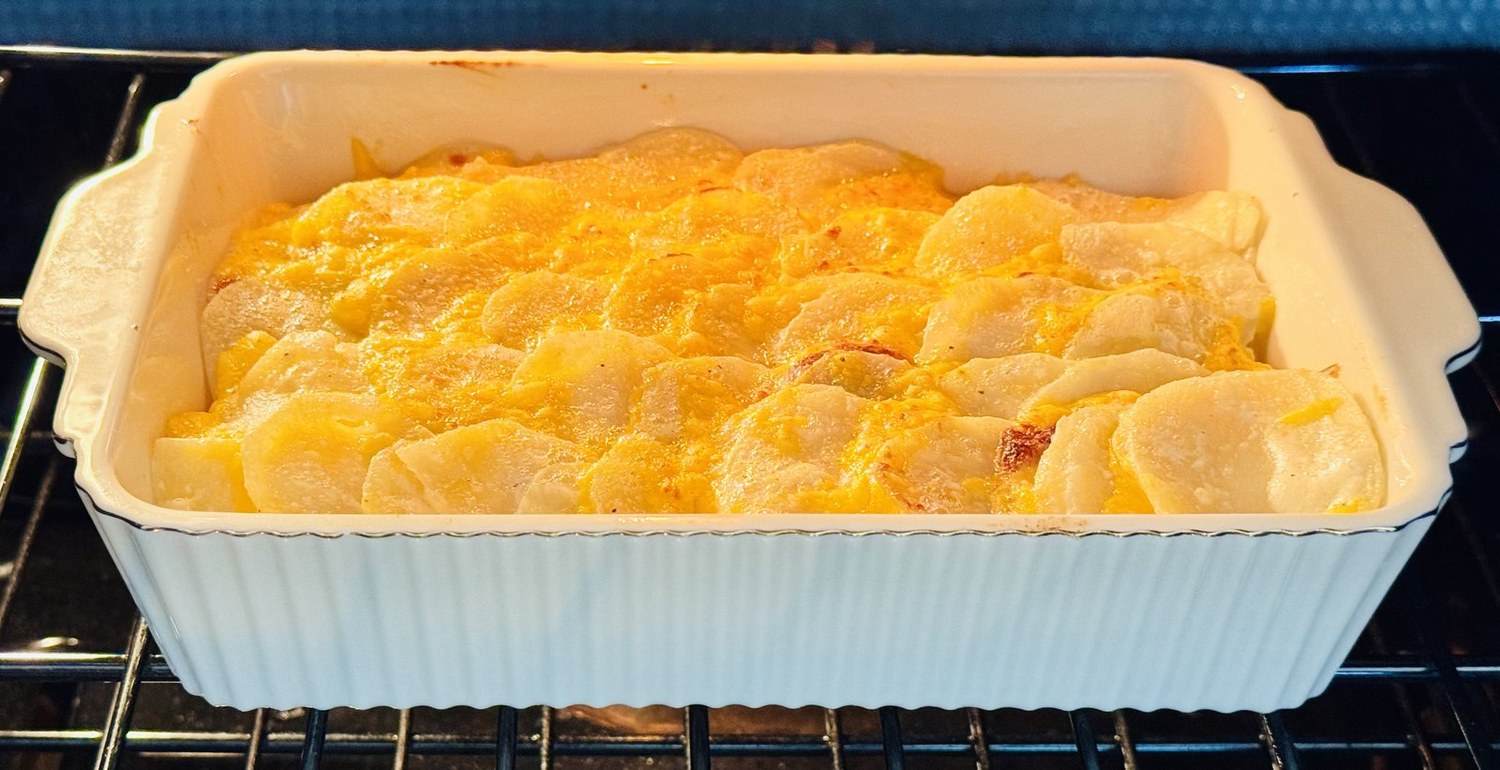 Scalloped potatoes browning under the broiler in a white baking dish