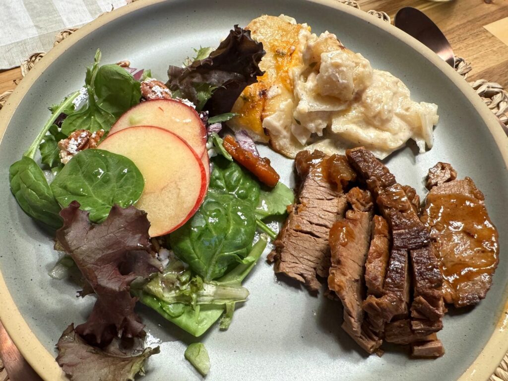 Dinner plate with scalloped potatoes, sliced brisket with gravy, and a fall salad with apple slices