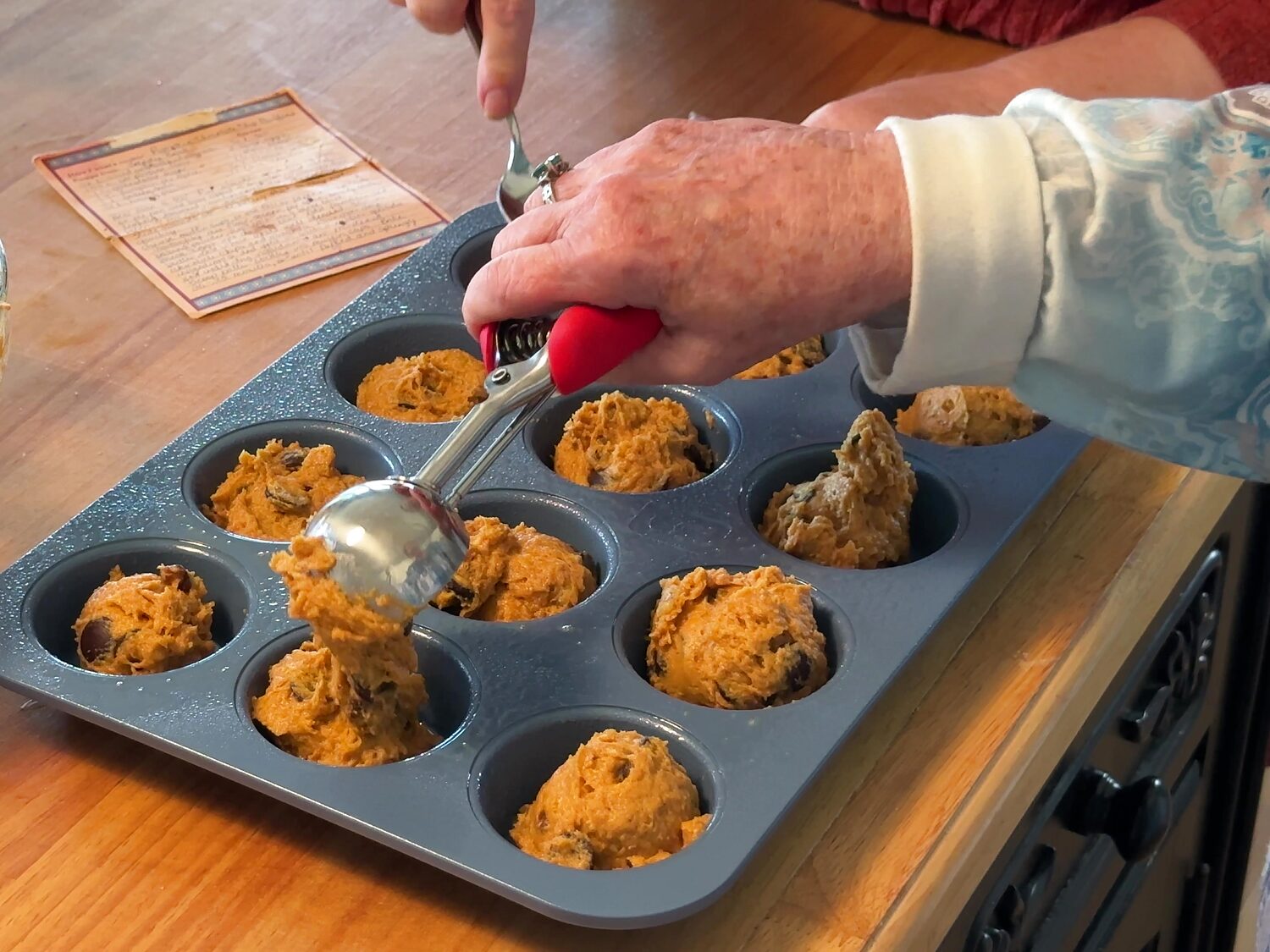 Using a spring-loaded scoop to fill a muffin pan with pumpkin chocolate chip batter