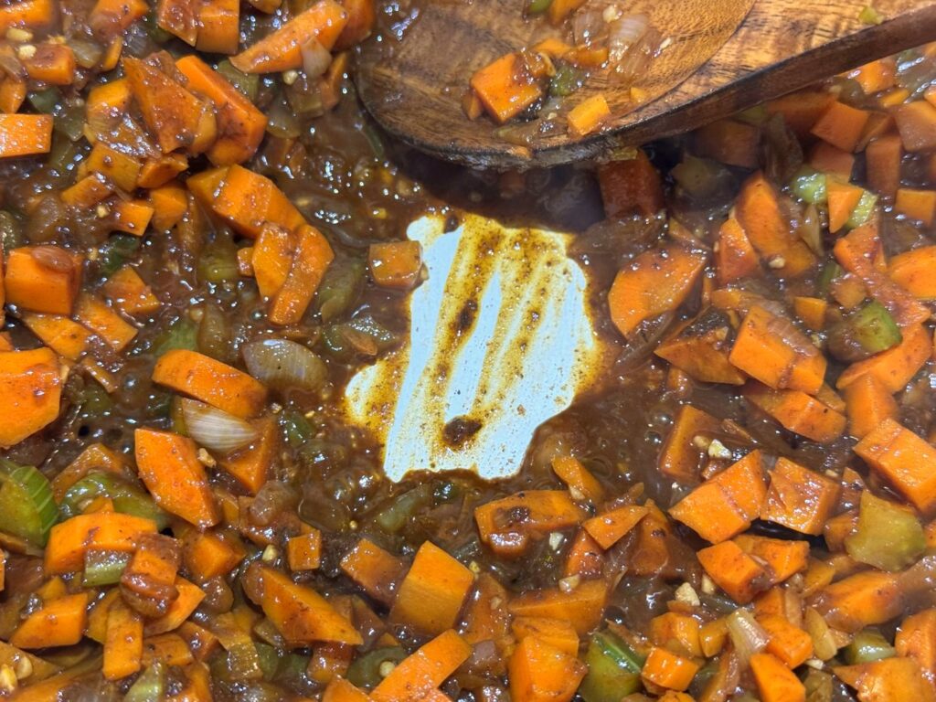 A wooden spoon scraping the browned bits off the bottom of a white Dutch oven