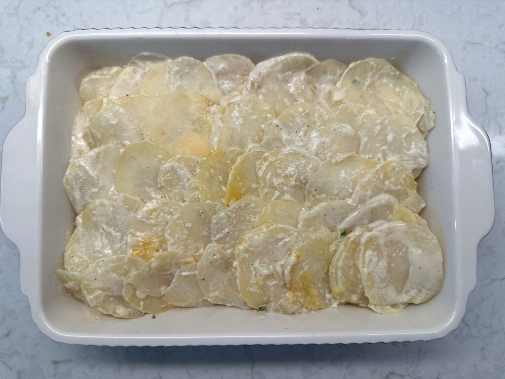 Thin potato slices shingled in overlapping rows on top of scalloped potatoes in a white baking dish