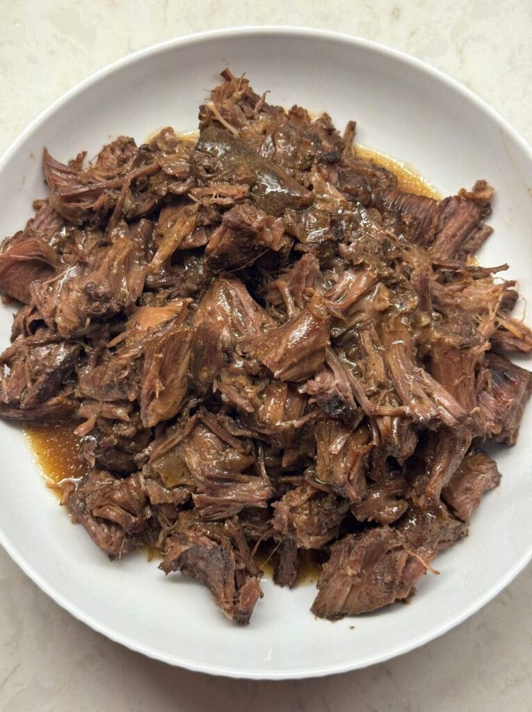 Shredded Mississippi pot roast stirred into its juices in a white bowl