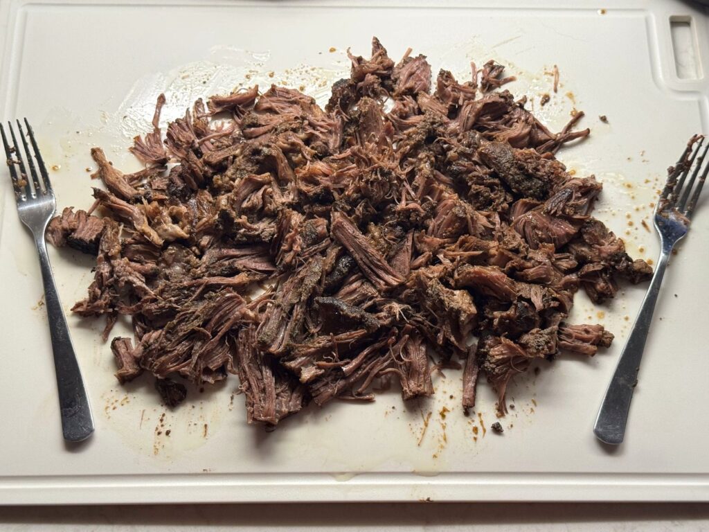 Shredded pot roast on a white cutting board with two forks