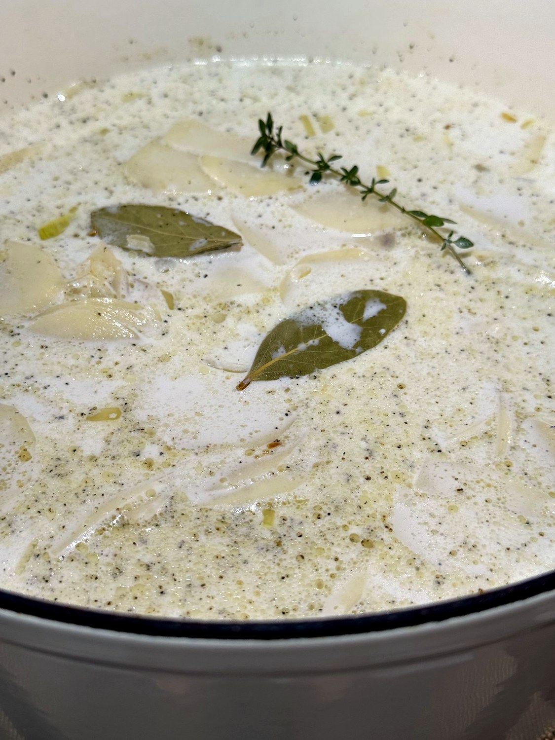 Sliced potatoes simmering in a creamy half-and-half sauce with bay leaves and a thyme sprig