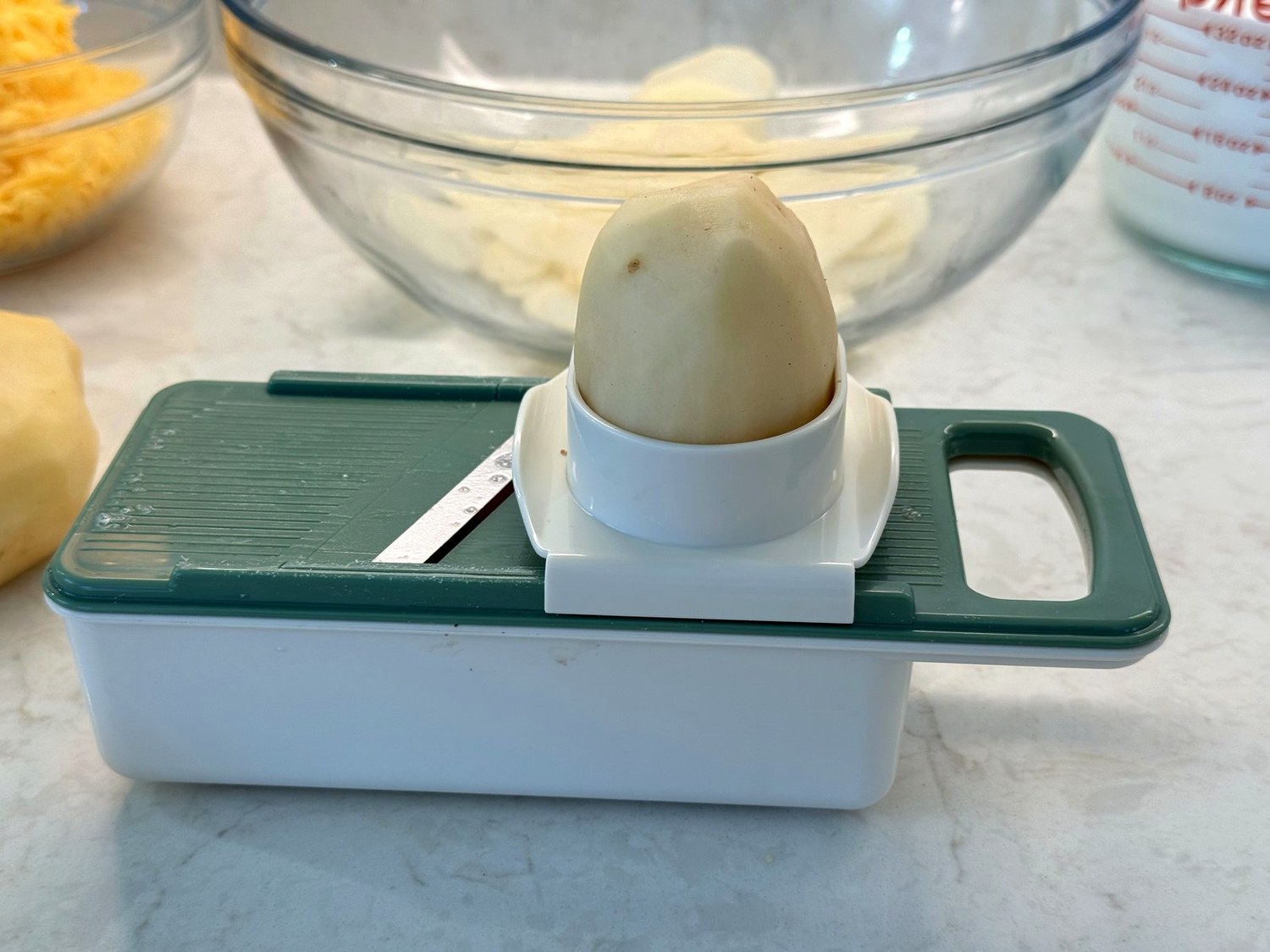 Peeled russet potato in the hand guard of a green mandoline slicer