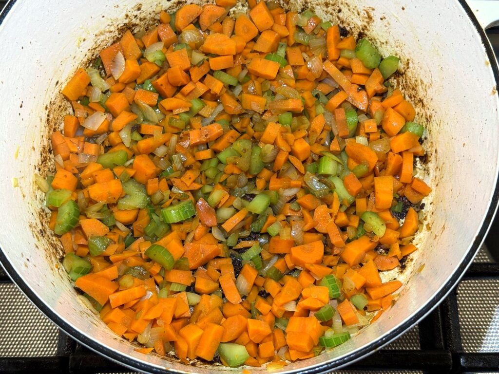 Diced carrots, celery, and onion added to a Dutch oven with browned bits on the bottom