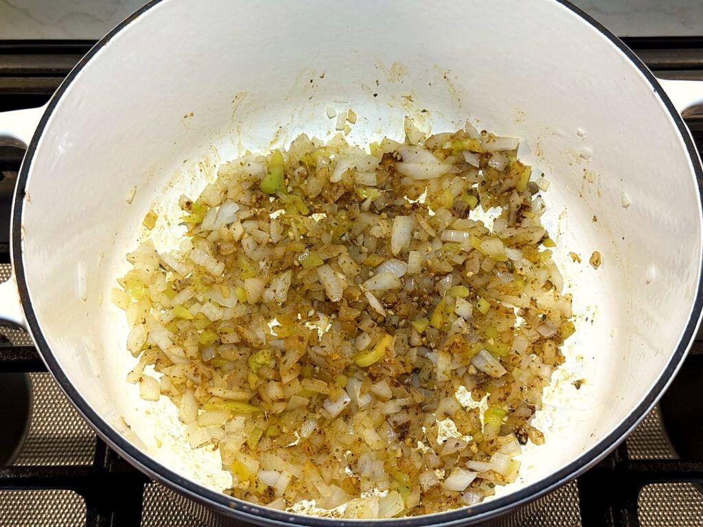 Onion and peppers coated in toasted spices in a white Dutch oven