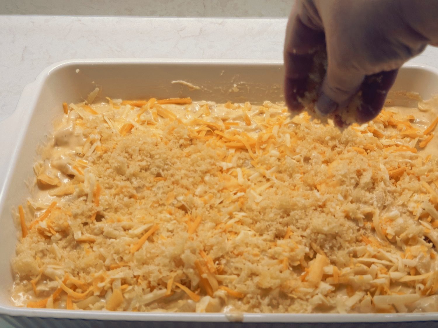 A hand sprinkling buttered panko crumbs over the cheese-topped mac and cheese