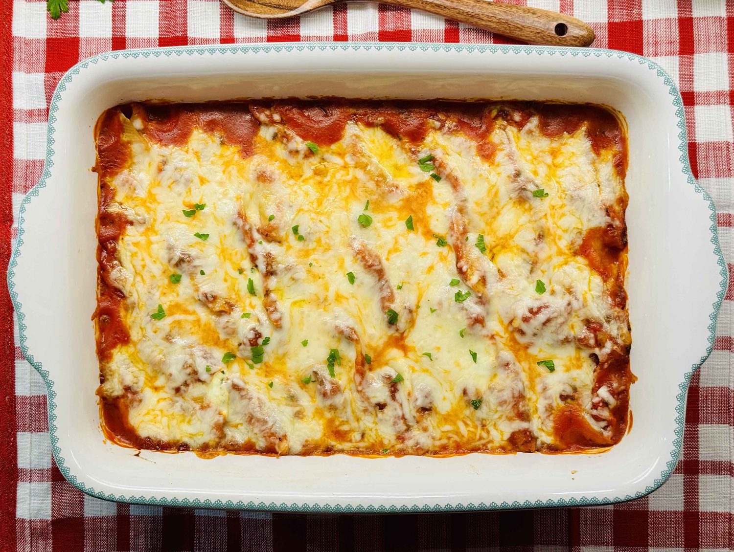 Baked stuffed shells with melted mozzarella and chopped parsley in a white baking dish on a red checked cloth