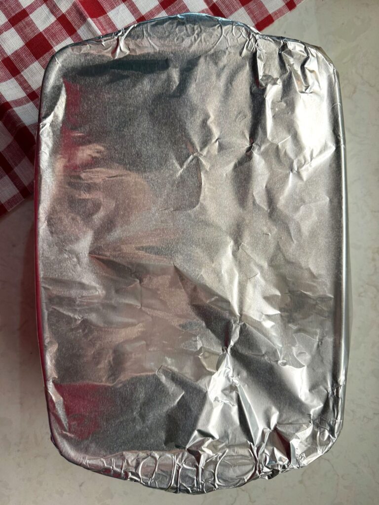 A baking dish of stuffed shells covered tightly with aluminum foil