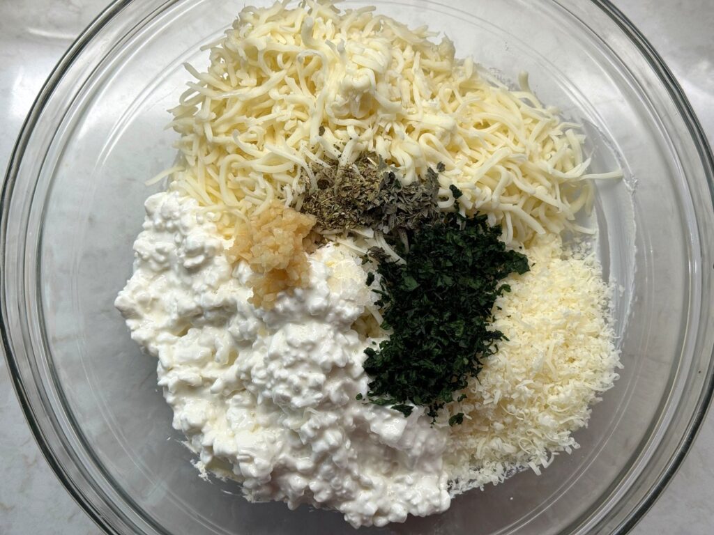 Cottage cheese, mozzarella, Parmesan, garlic, chopped parsley, and dried herbs in a glass mixing bowl