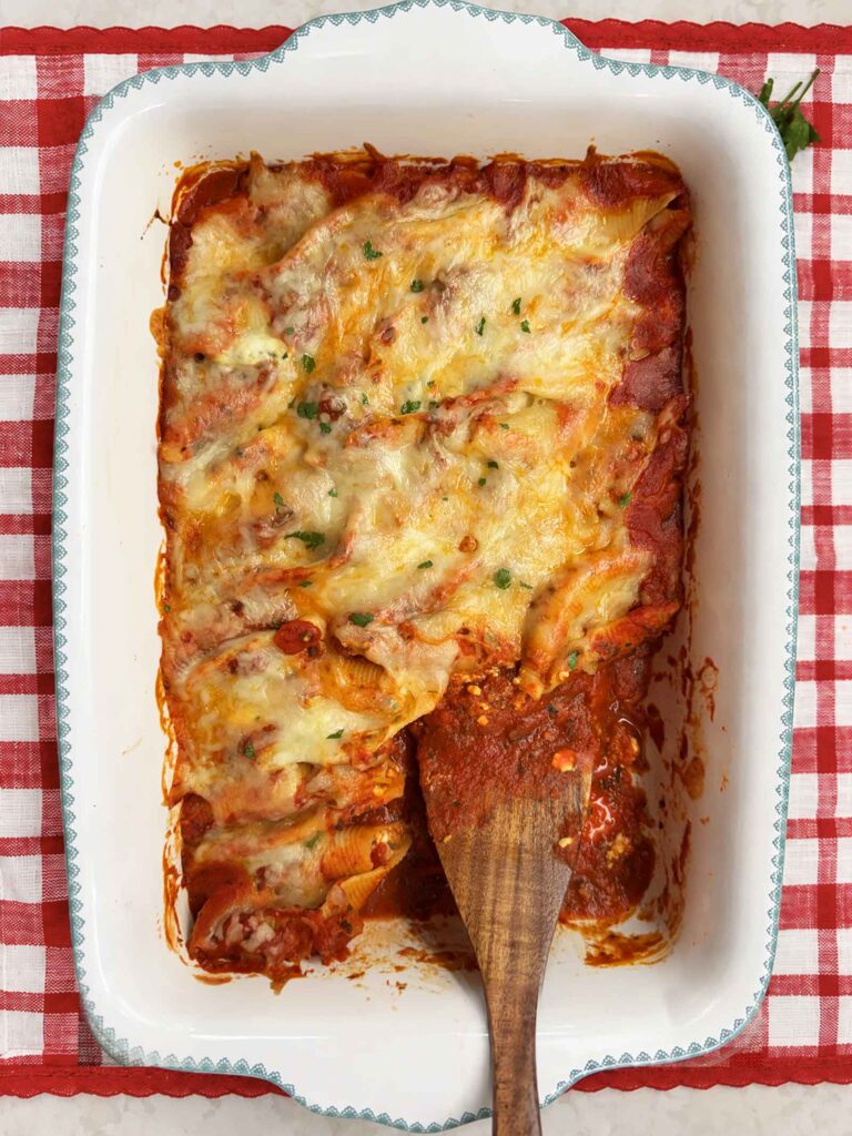 A pan of stuffed shells with a dinner portion missing and a messy spatula