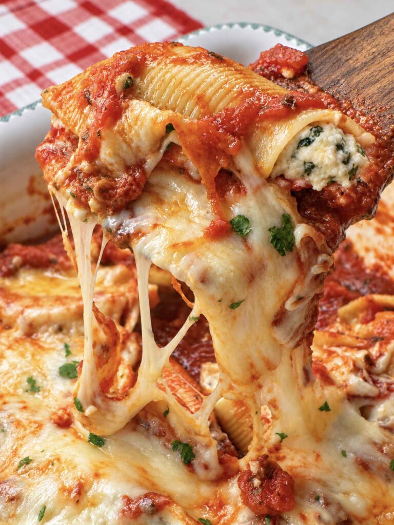 A baked stuffed shell lifted from the pan with a wooden spatula, trailing strings of melted mozzarella