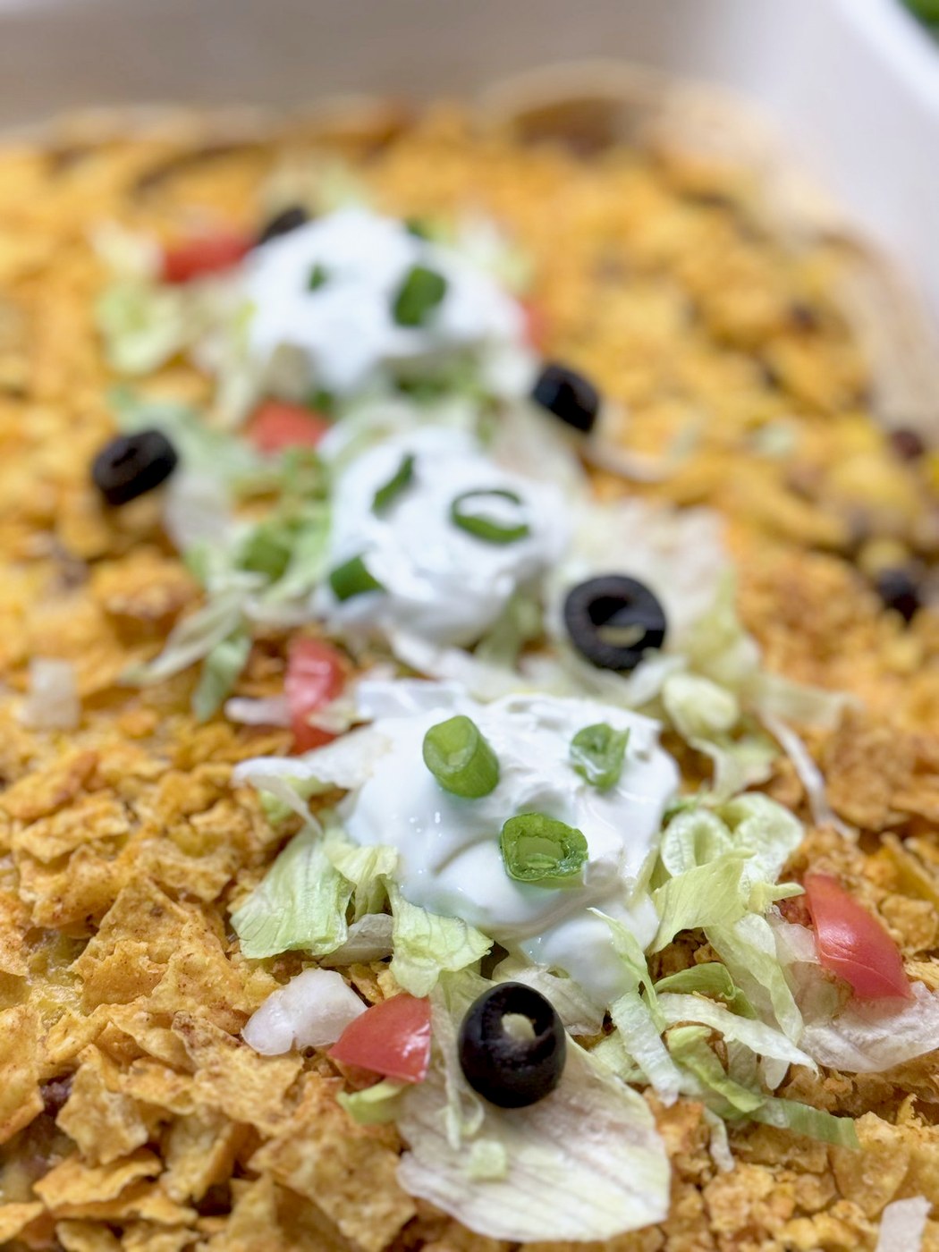 Close-up of taco casserole topped with sour cream, shredded lettuce, diced tomato, green onion, black olives, and cilantro