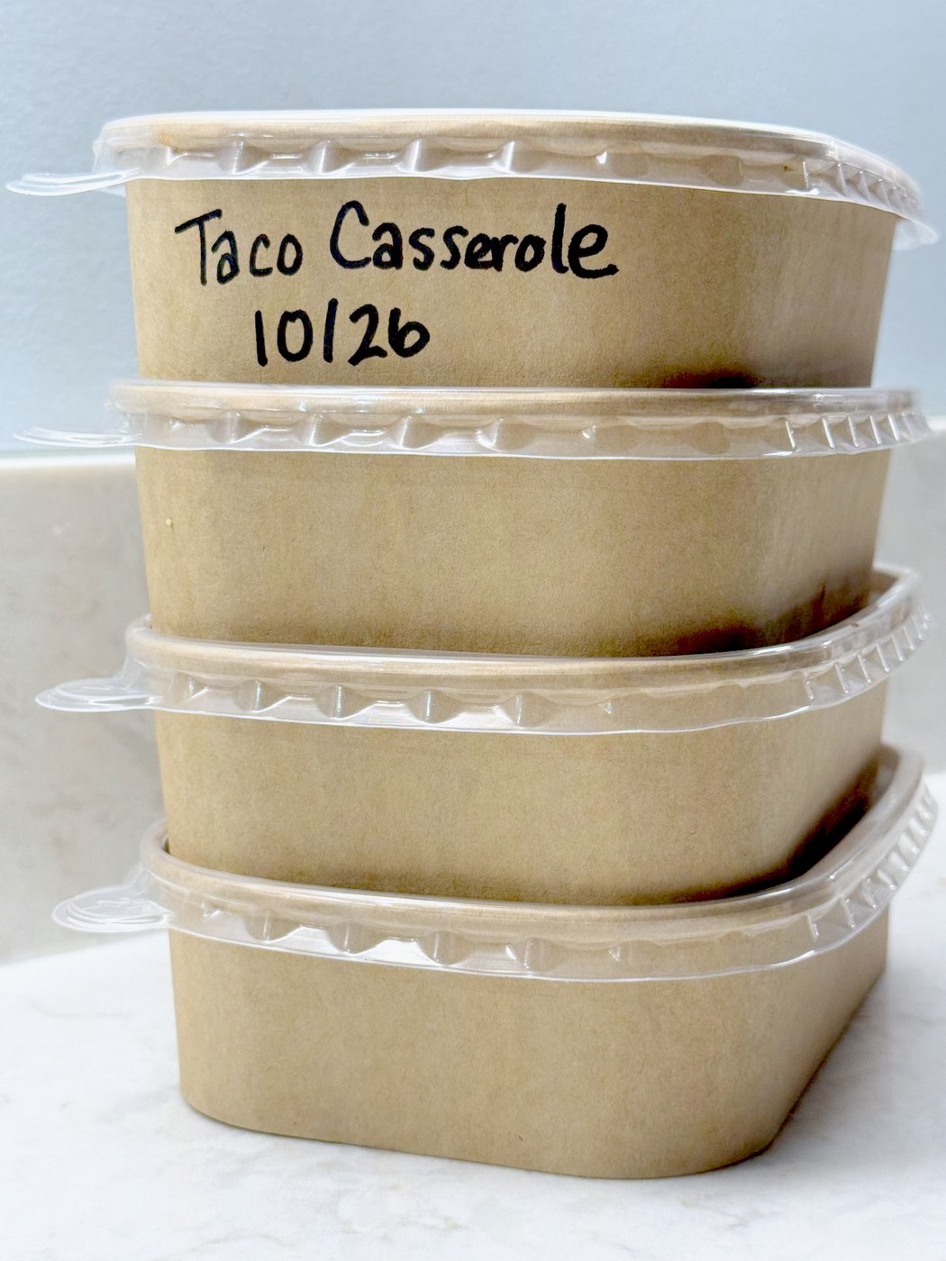Four individual containers of leftover taco casserole stacked and labeled with the name and date