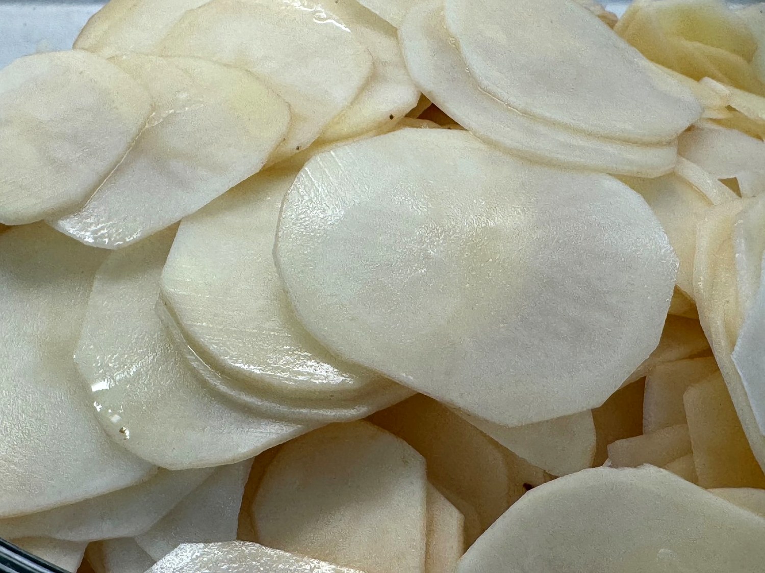 Thin, round slices of peeled russet potatoes in a glass bowl