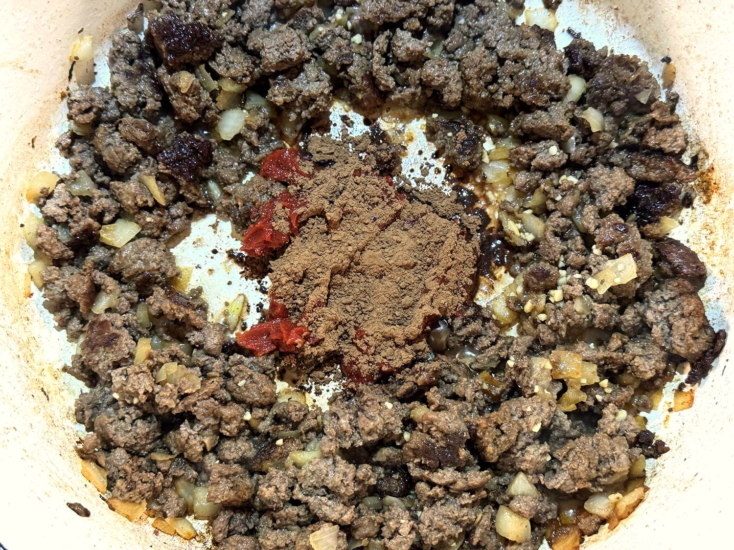 Tomato paste and cocoa powder in the center of the pot with browned ground venison, onion, and garlic