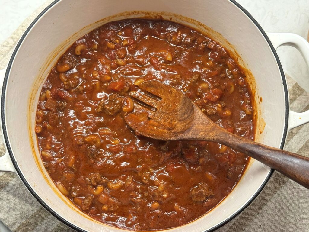 Thick venison goulash with tender elbow macaroni in a Dutch oven with a wooden spoon