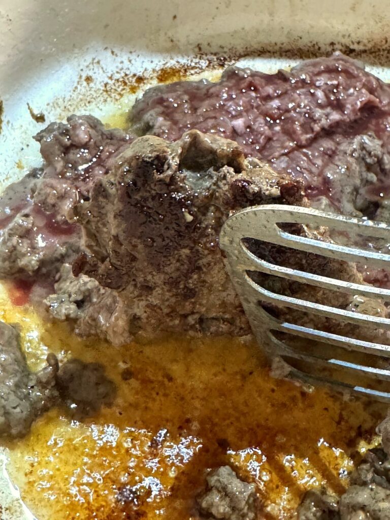 A spatula flipping a section of seared ground venison to show the dark brown crust underneath