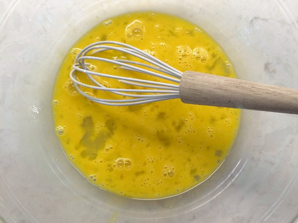 Two whisked eggs in a large glass mixing bowl with a whisk