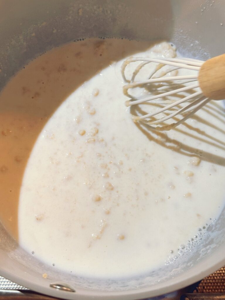 Whisking the warm milk into the roux in a saucepan