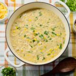 A big pot of white chicken chili with bowls of toppinsg containing with shredded cheddar, sour cream, and cilantro
