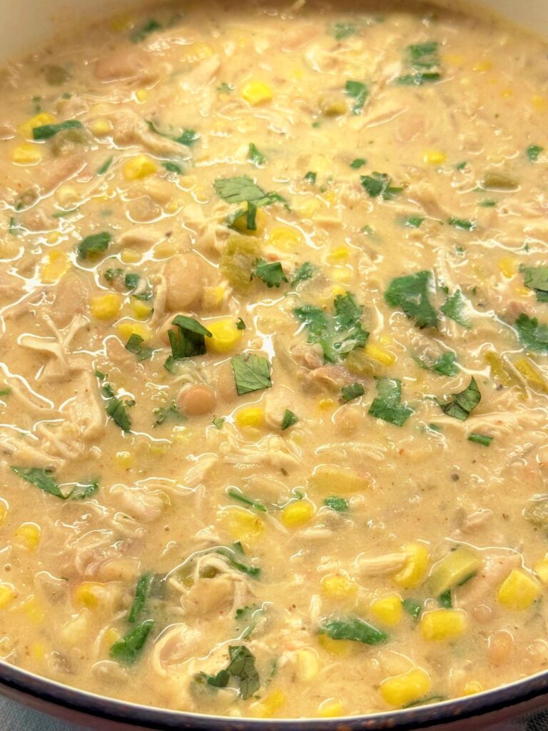 Close-up of creamy white chicken chili with shredded chicken, white beans, corn, and cilantro