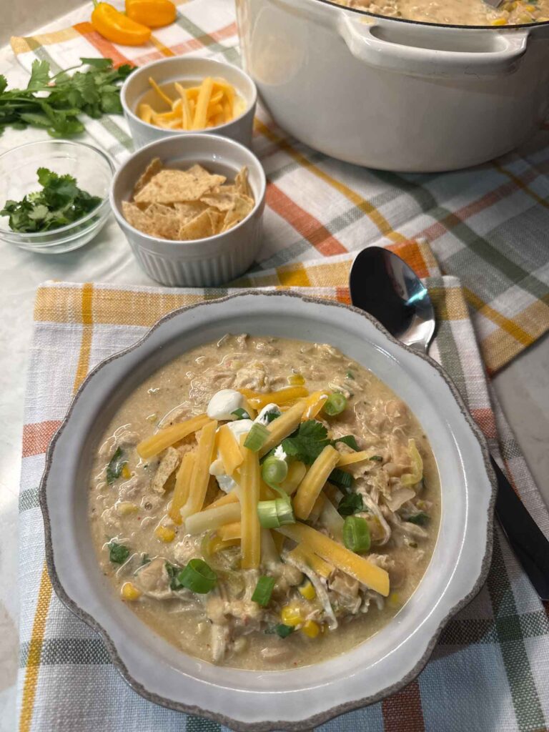 An everyday photo of a gray bowl of white chicken chili topped with shredded cheddar, sour cream, and cilantro