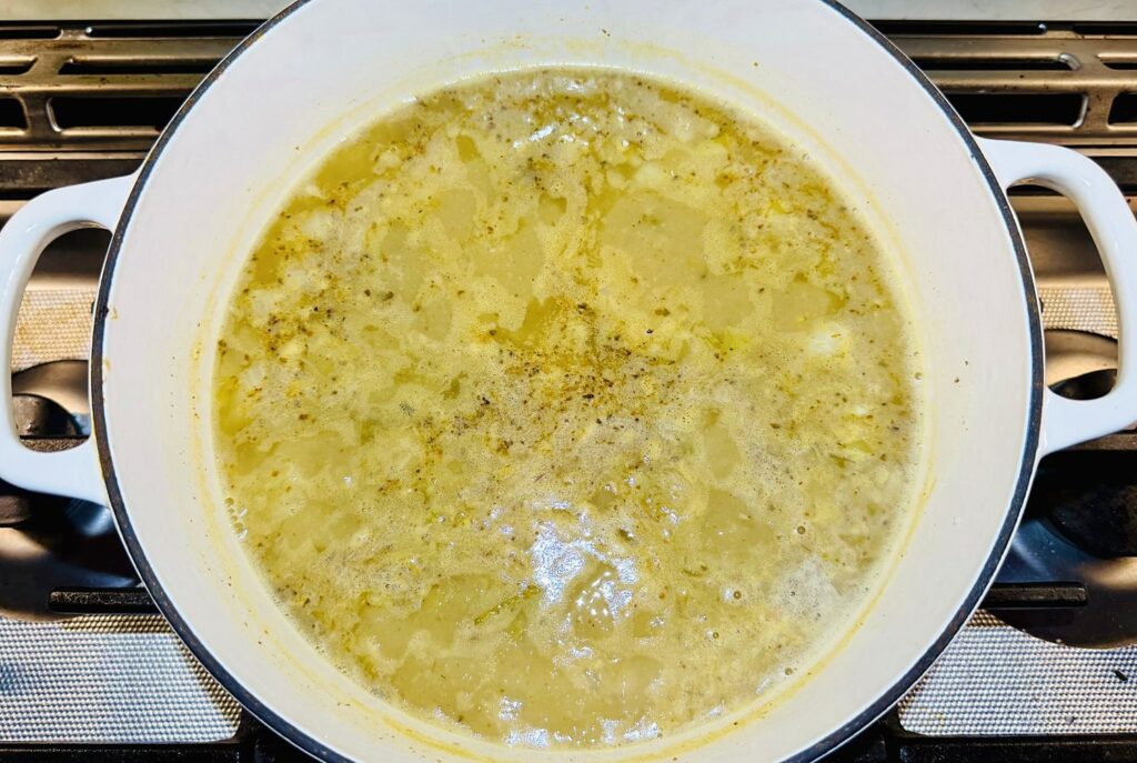 White chicken chili base simmering in a white Dutch oven on a gas stove